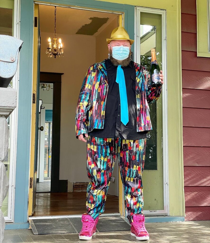 Chaz wearing the most fabulous outfit accompanied by a fancy champagne bottle in front of his new house on Keys Day™